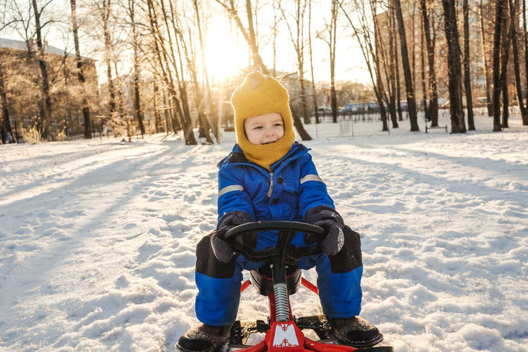 Full length of boy sitting on toy outdoors during winter
