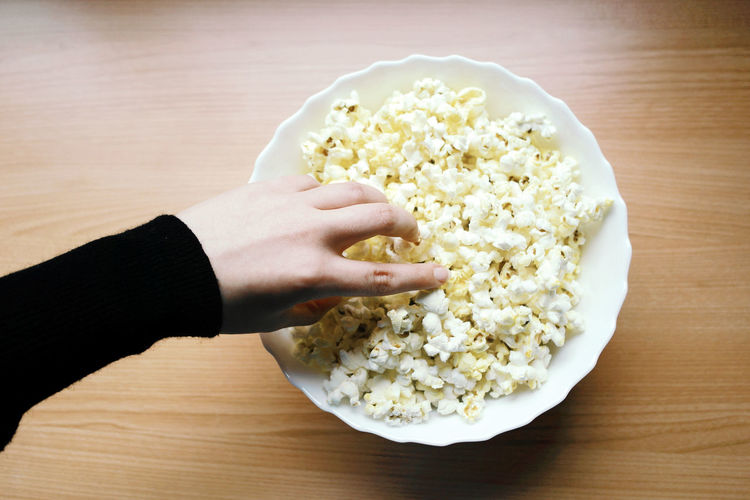 Cropped hand having popcorn on table