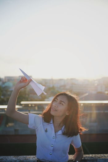 Woman flying paper airplane against sky