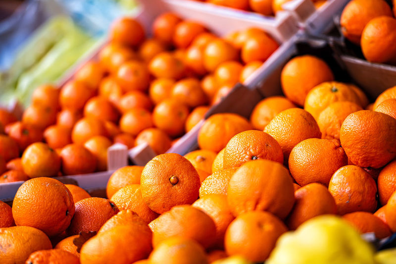 Rows of ripe mandarins, oranges and other fruits in wooden boxes on the market, closeup