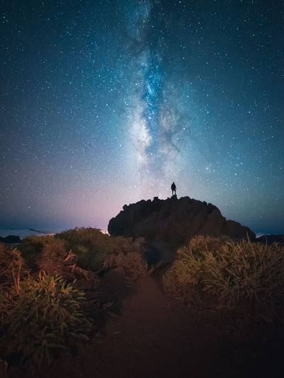 Back view of unrecognizable traveler male standing on hill while admiring spectacular scenery of milky way over mountainous in starry night