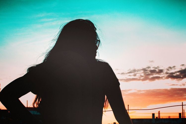 Rear view of silhouette girl standing against sky during sunset