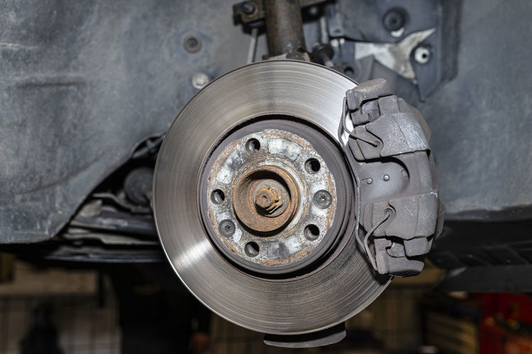 Front brake discs with brake caliper and brake pads in the car, on a car lift in a workshop.