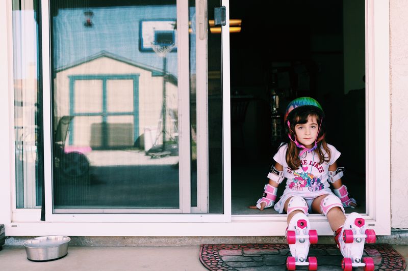 Full length of girl wearing roller skate while sitting in doorway