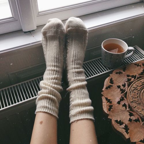 Low section of person wearing socks by tea cup on radiator at home