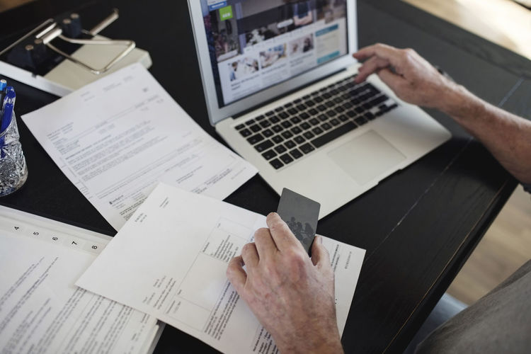 Cropped image of senior man with bills doing online payment at home