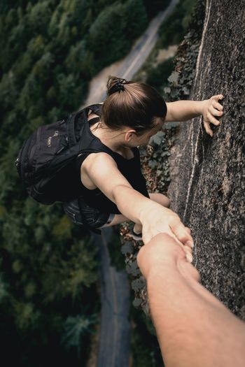 Cropped hand holding young backpack woman climbing on cliff