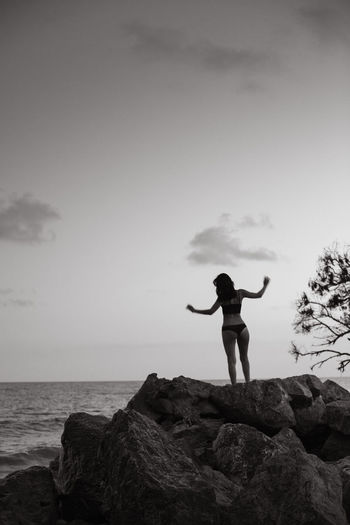 Woman standing on rock by sea against sky