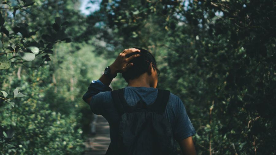 Full length of teenage man standing by tree in forest alone and stressed