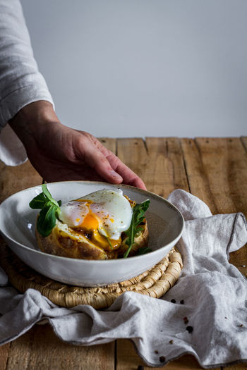 Crop anonymous hand holding dish with fried egg on potato on wooden table with fried mushrooms grated cheese and herbs