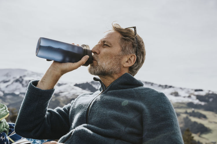 Mature man drinking water against sky at salzburger land, austria