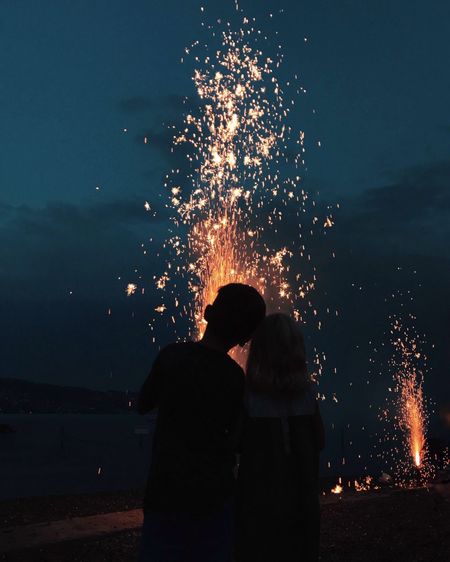 Man and woman looking at firework display against sky
