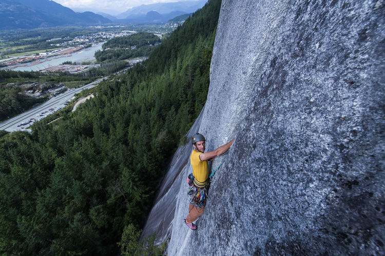 Man rock climbing on squamish chief looking at camera city background