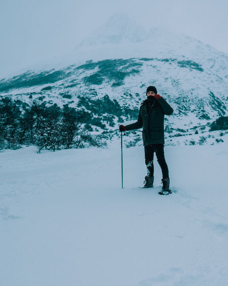 Full length portrait of man standing on snow against mountain and sky