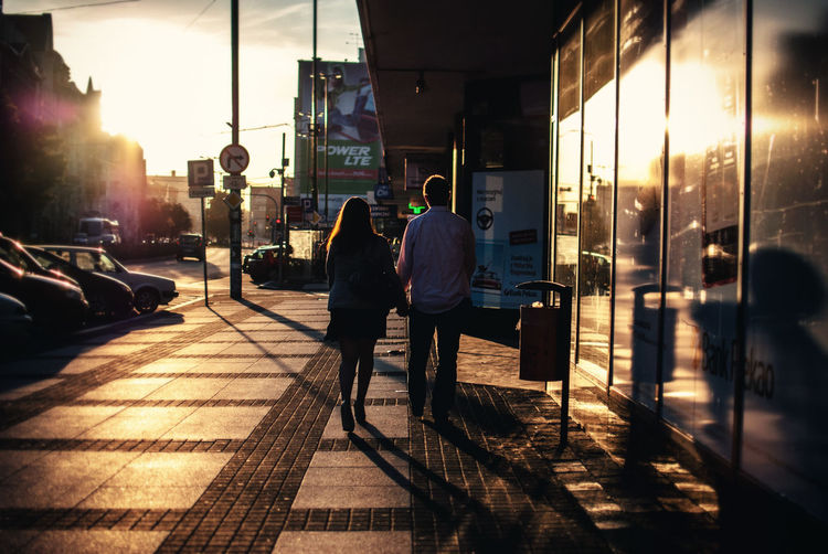 Rear view of couple walking on sidewalk in city