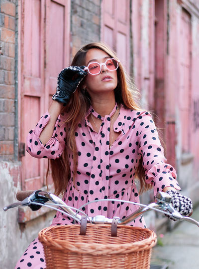Portrait of model in pink dress and gloves on a bicycle in london