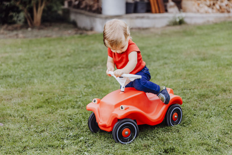 Baby girl sitting on red toy car in lawn