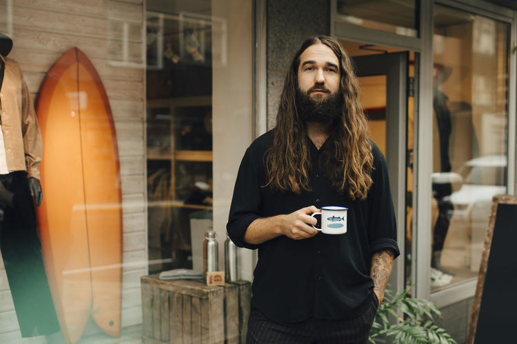Portrait of male entrepreneur with coffee cup against clothing store