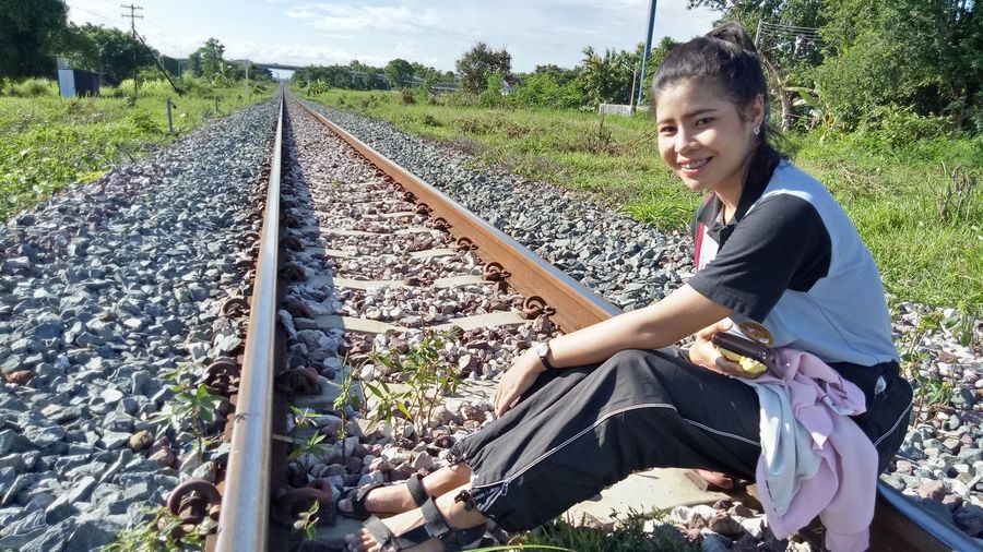 Full length portrait of smiling young woman sitting on railroad track
