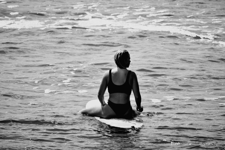Rear view of woman sitting on surfboard in sea