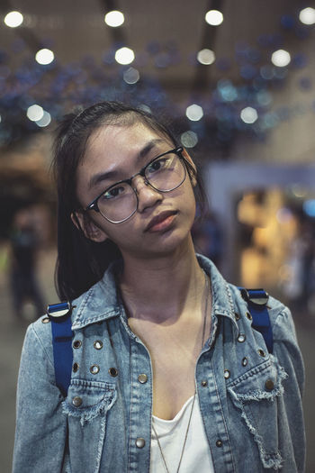 Close-up portrait of teenage girl wearing eyeglasses against defocused lights