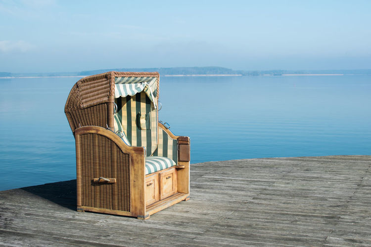 Hooded beach chair on pier against sea