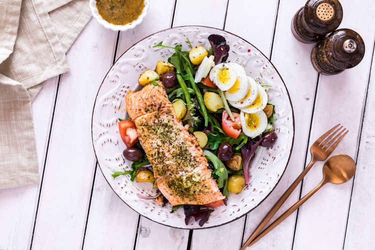 A top down view of a salmon nicoise salad on a rustic table, ready for eating.