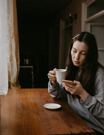 Freelance woman with the coffee and mobile phone at home talking expressive