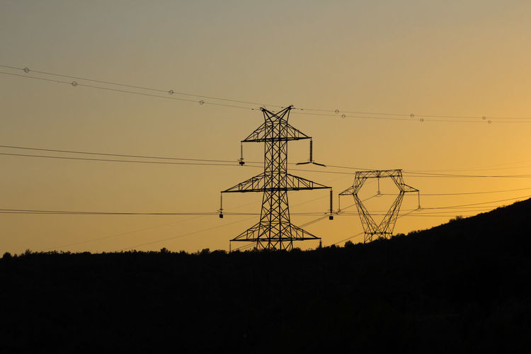 Silhouette electricity pylons against clear sky during sunset