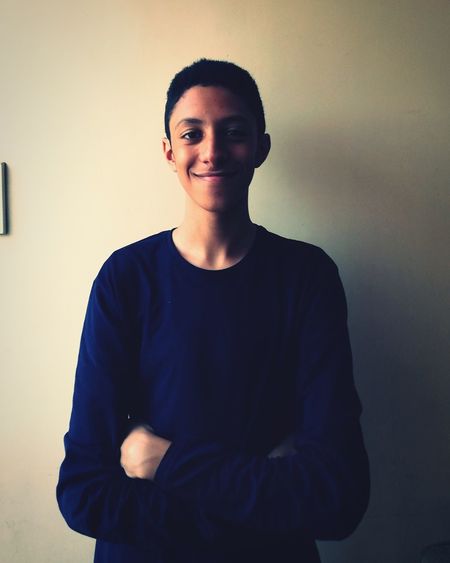 Portrait of smiling teenage boy with arms crossed standing against wall