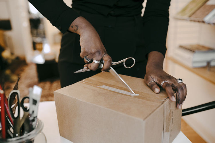 Midsection of businesswoman opening package with scissors at home office