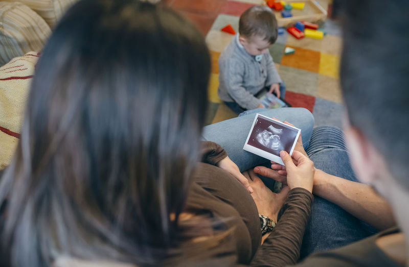 Parents holding ultrasound while son using digital tablet in living room at home