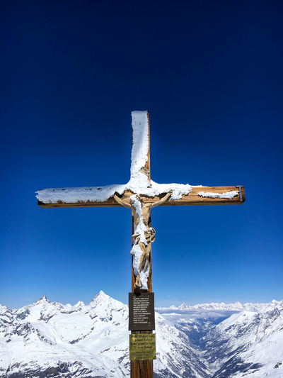 Snow covered cross with a wooden figure of jesus christ at peak of klein matterhorn mountain