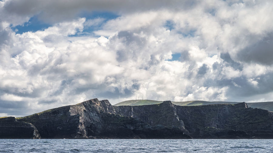 Tall kerry cliffs with dramatic sky, seen from a boat on atlantic ocean on a summer day, ireland