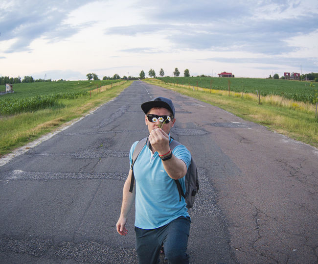 Portrait of young man standing on road against sky