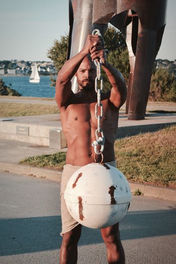 Full length of shirtless man holding ball while standing on road