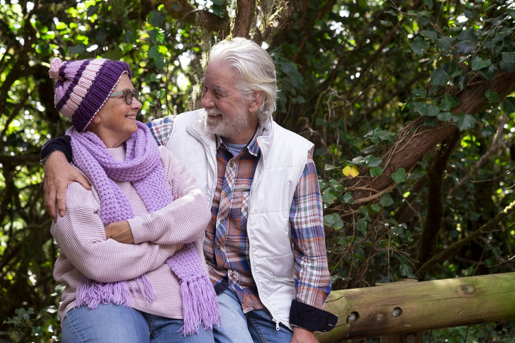 Smiling senior couple sitting by tree outdoors