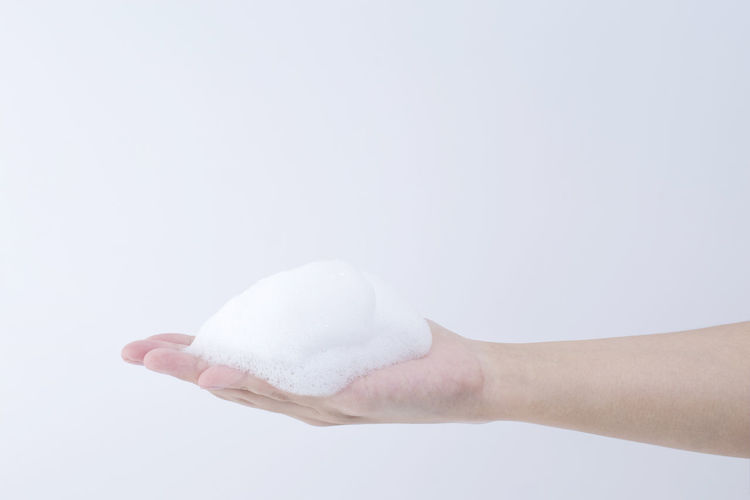 Close-up of hand holding bubbles over white background