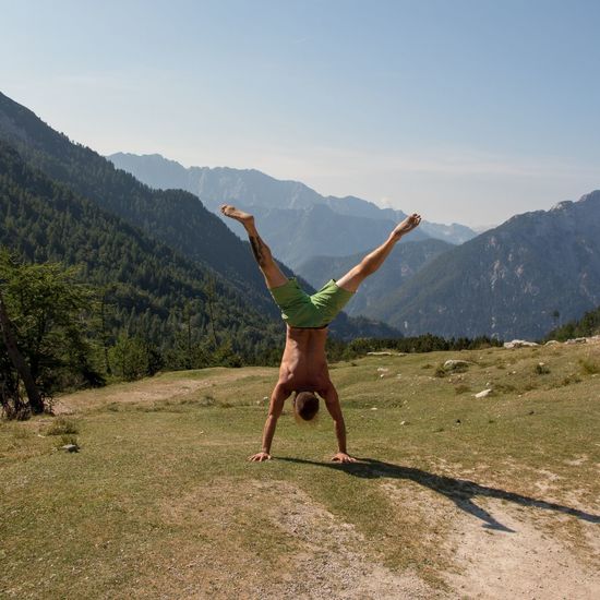 Full length rear view of shirtless man doing handstand on mountain during sunny day