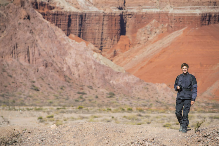 Man in motorcycle gear, standing in front of red sandstone formations