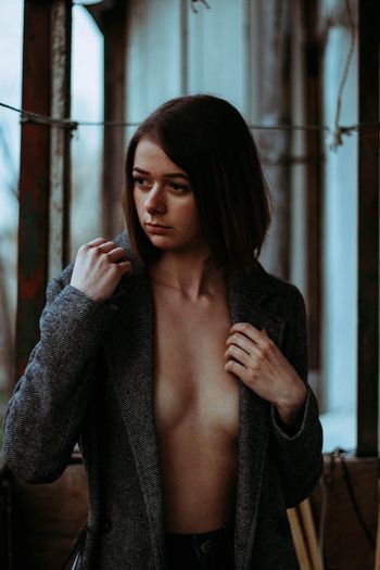 Thoughtful seductive woman wearing unbuttoned overcoat while looking away at home