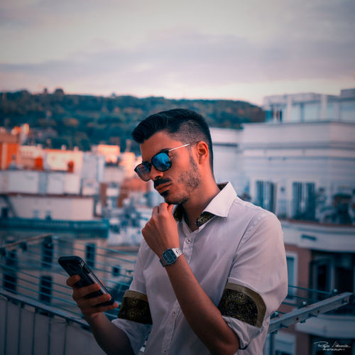Young man using mobile phone while standing against cityscape