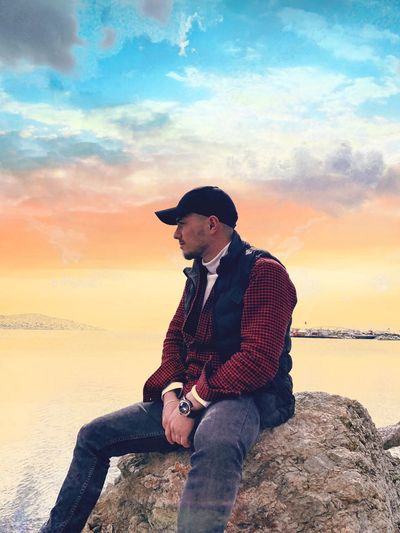 Young man sitting on rock against sea during sunset