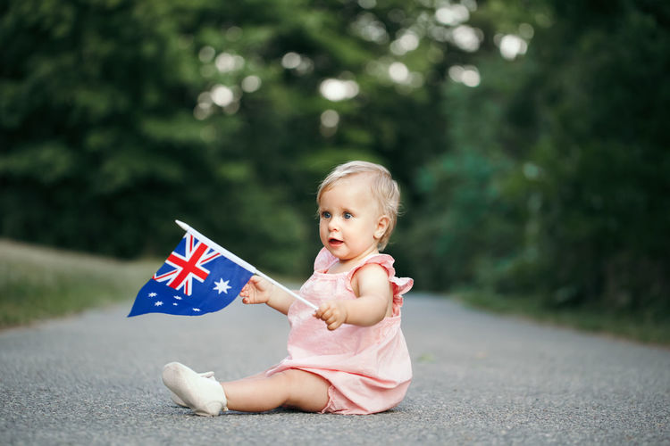 Cute girl holding australian flag sitting on road