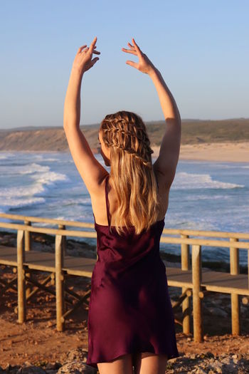 Rear view of woman standing at beach against sky