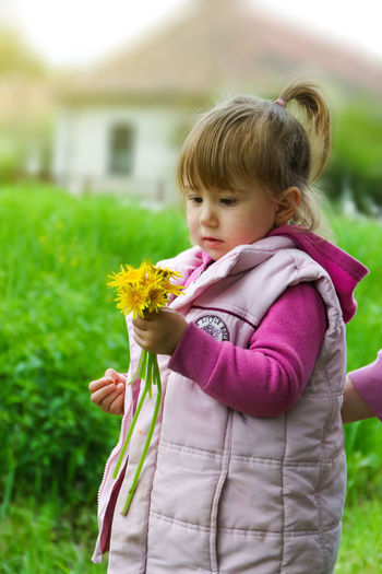 Cute girl with yellow flowers standing on field