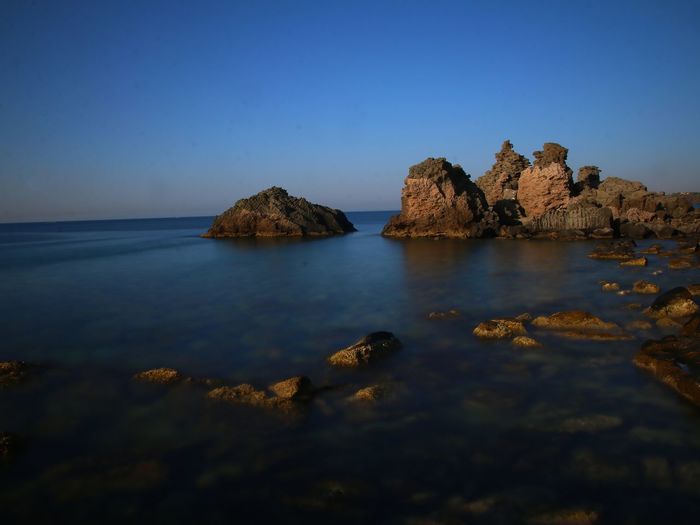 Scenic view of rock formations in sea against clear blue sky