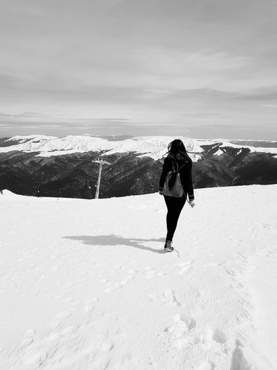 Rear view of woman walking on snow covered landscape against sky