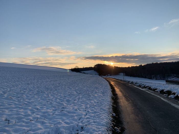 Snow covered land road against sky during sunset