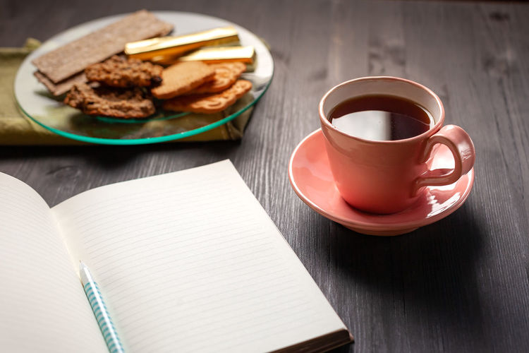 Empty notebook, cup of tea and cookies on black background